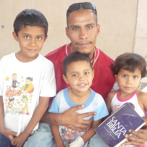 Mario holding his Bible and embracing his kids, Chuy and America, and his younger brother, Ismael.